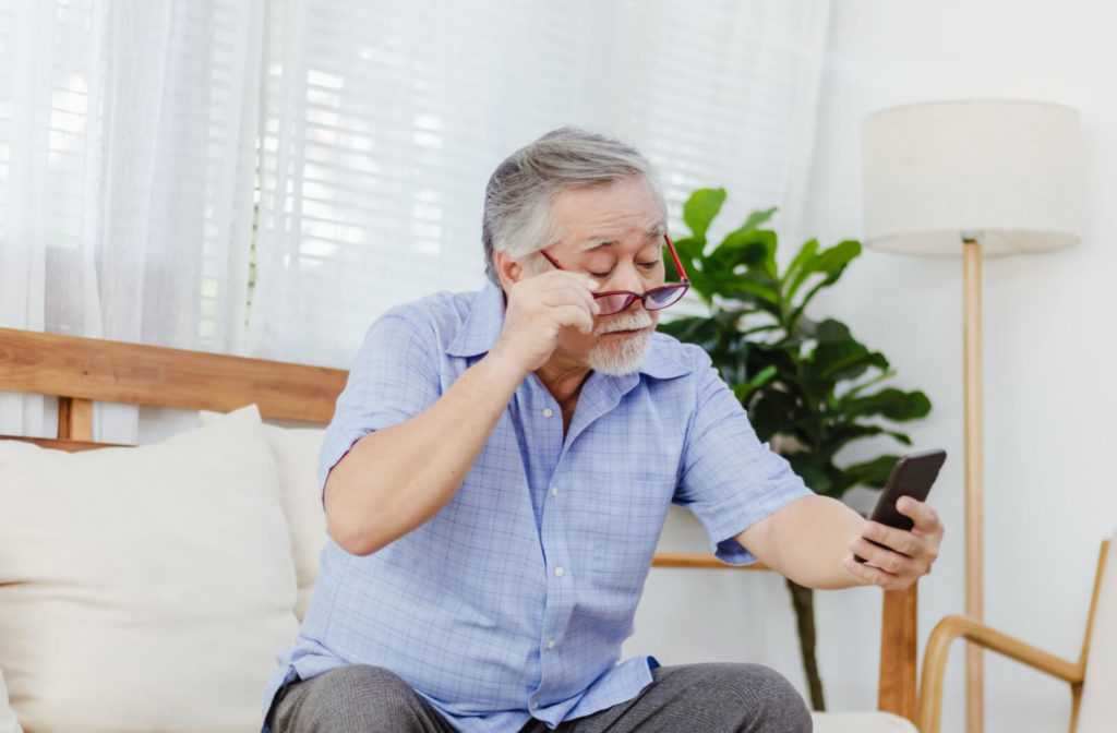 A senior man sitting and holding a smartphone is unable to read clearly due to farsightedness