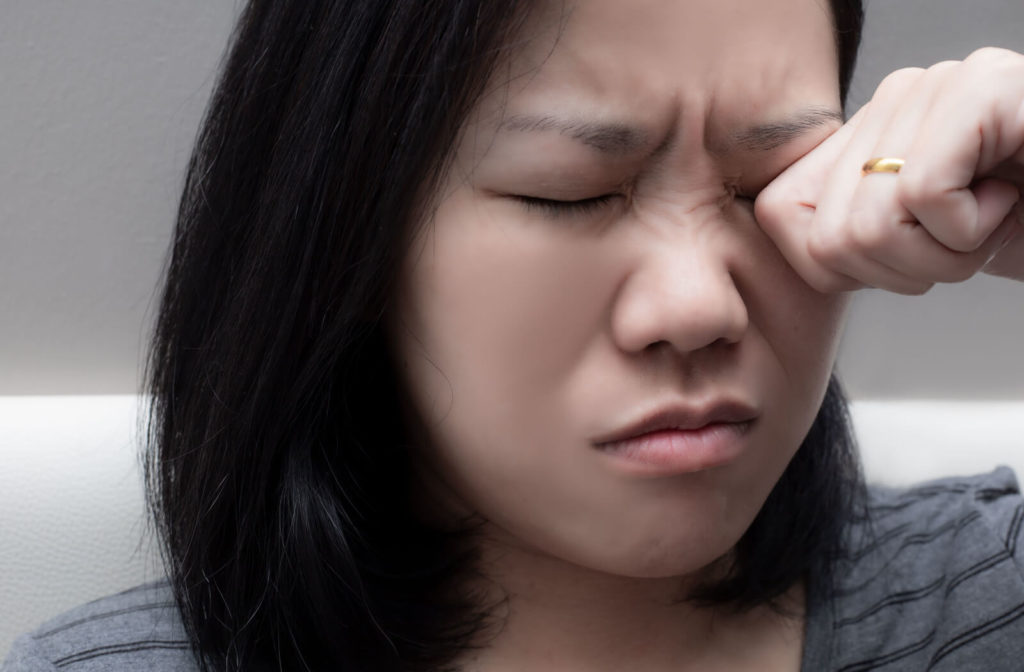 A woman with both eyes close, rubbing her left eye with her left hand