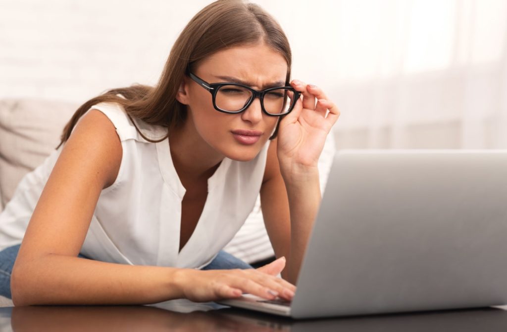 A woman adjusting her glasses and leaning closer to her laptop to see its content better.