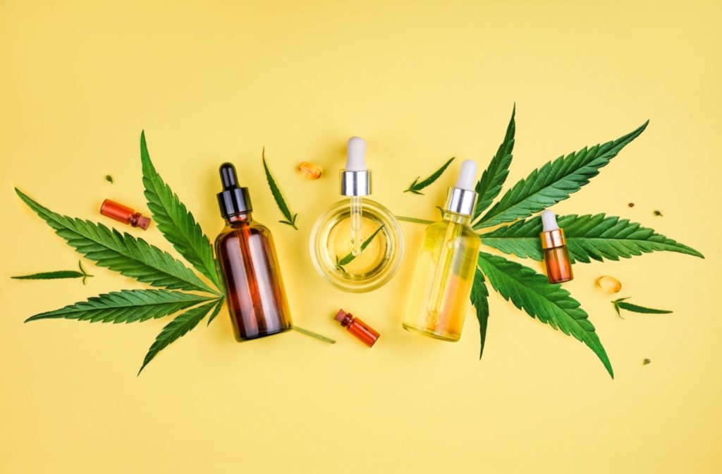 An assortment of CBD oil products and cannabis leaves against a yellow background.