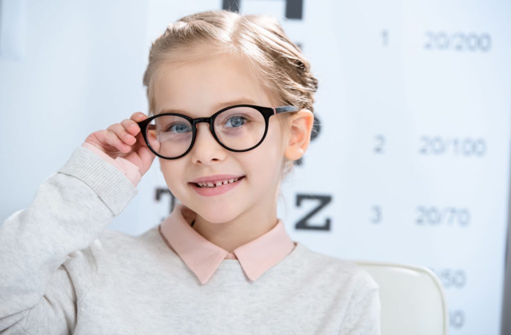 A young girl wearing myopia control glasses while standing in front of a Snellen eye chart