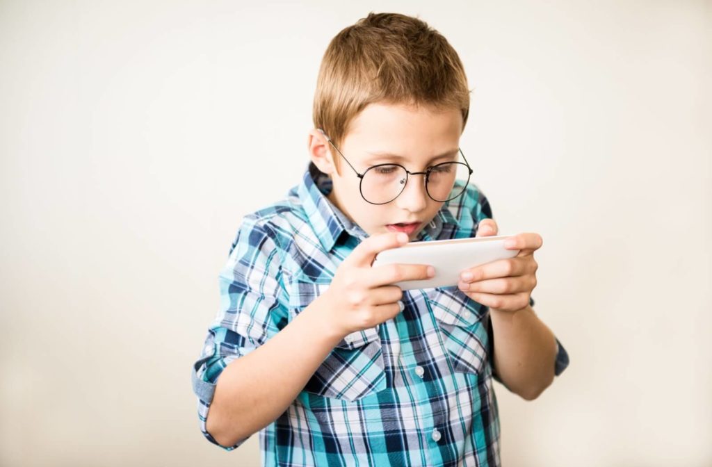 A child with glasses holding a smartphone very close to his face