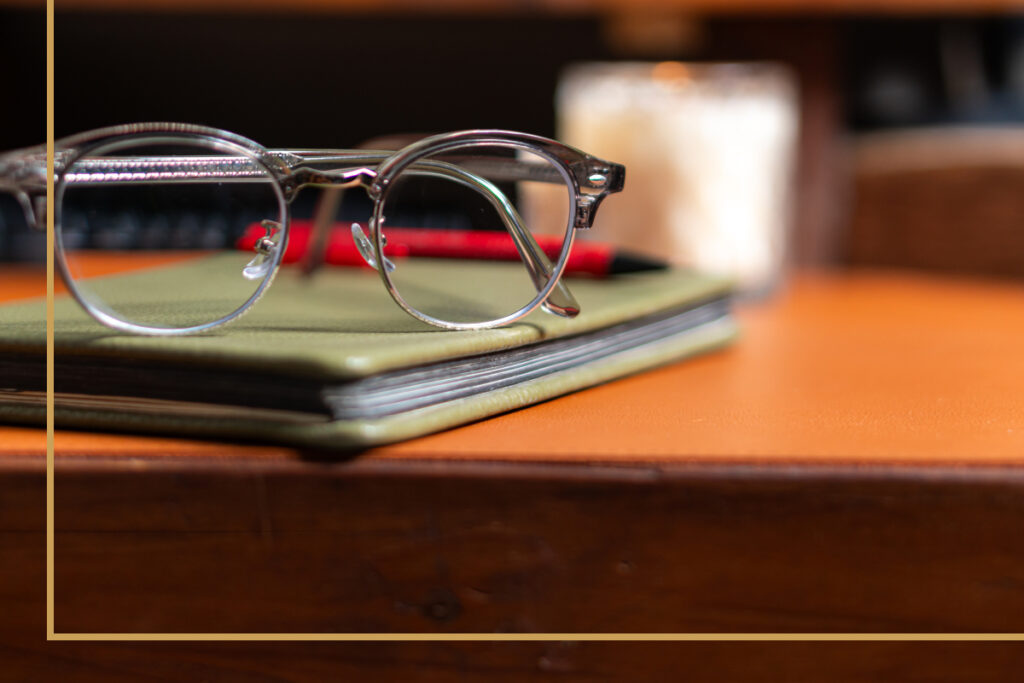 A pair of eyeglasses resting on a book atop a wooden desk, symbolizing the clarity and focus that prescription glasses provide over generic readers.